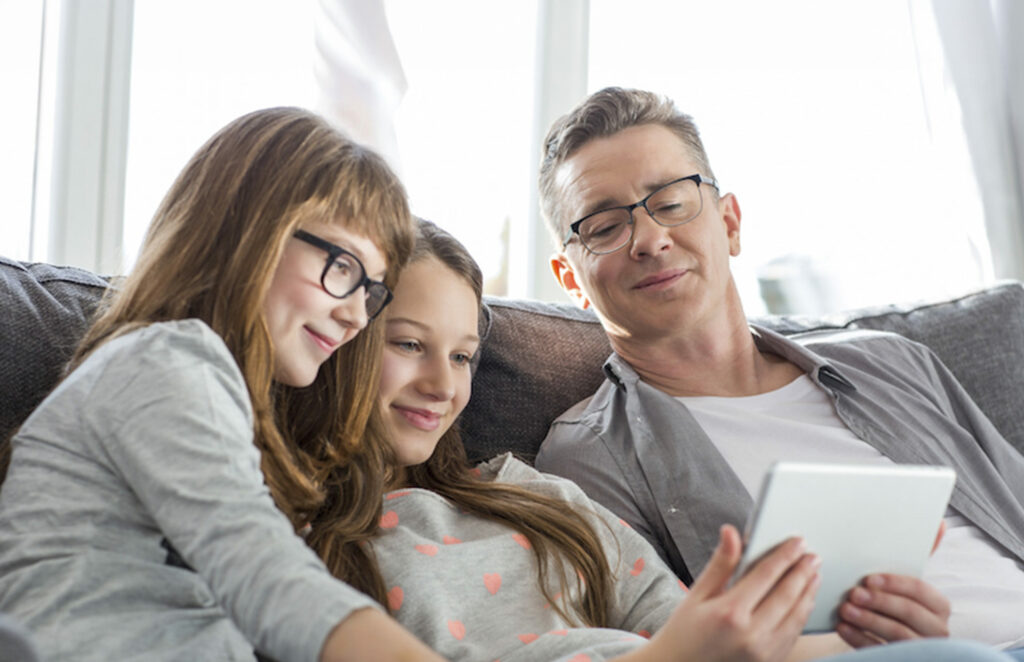 Père de famille partageant un contenu sur tablette avec ses filles